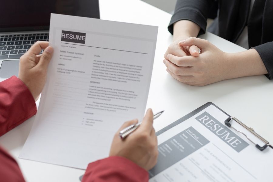 Két ember ül egy asztalnál interjúhelyzetben, egyikük önéletrajzokat tart a kezében. A kép az önéletrajz automatikus kiértékelése és HR szűrés folyamatának szemléltetésére alkalmas, amely kiemeli a toborzás automatizálásának és AI toborzásnak fontosságát irodai környezetben.